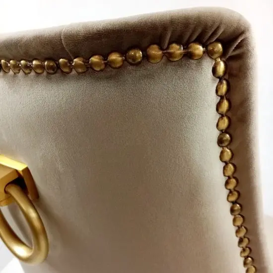 Close-up of an upholstered chair backrest with decorative golden trim and a ring handle